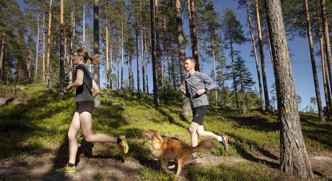 en tjej och en kille springer i skogen med sin hund