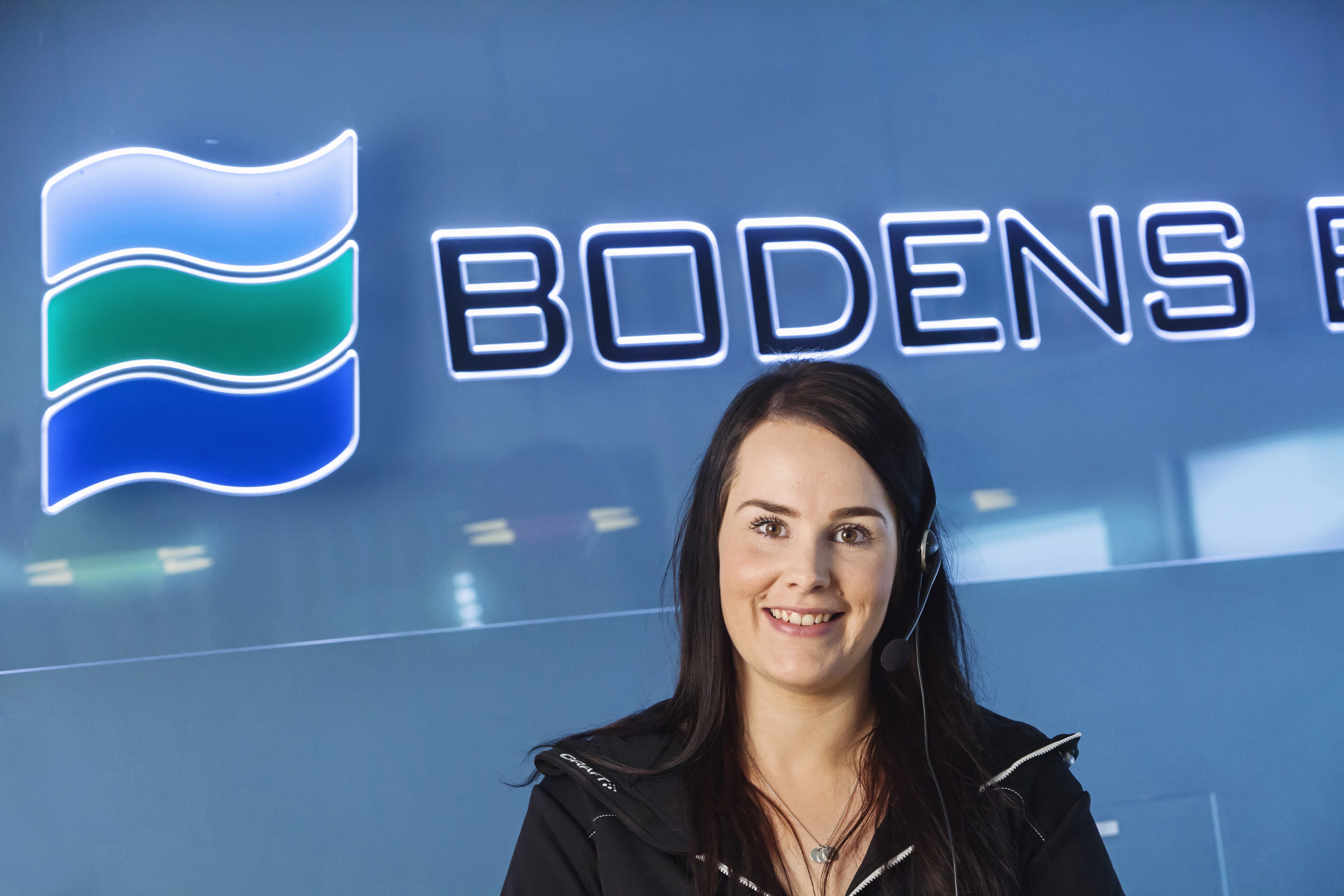 Tjej med telefonheadset framför blå vägg med Boden Energis logga