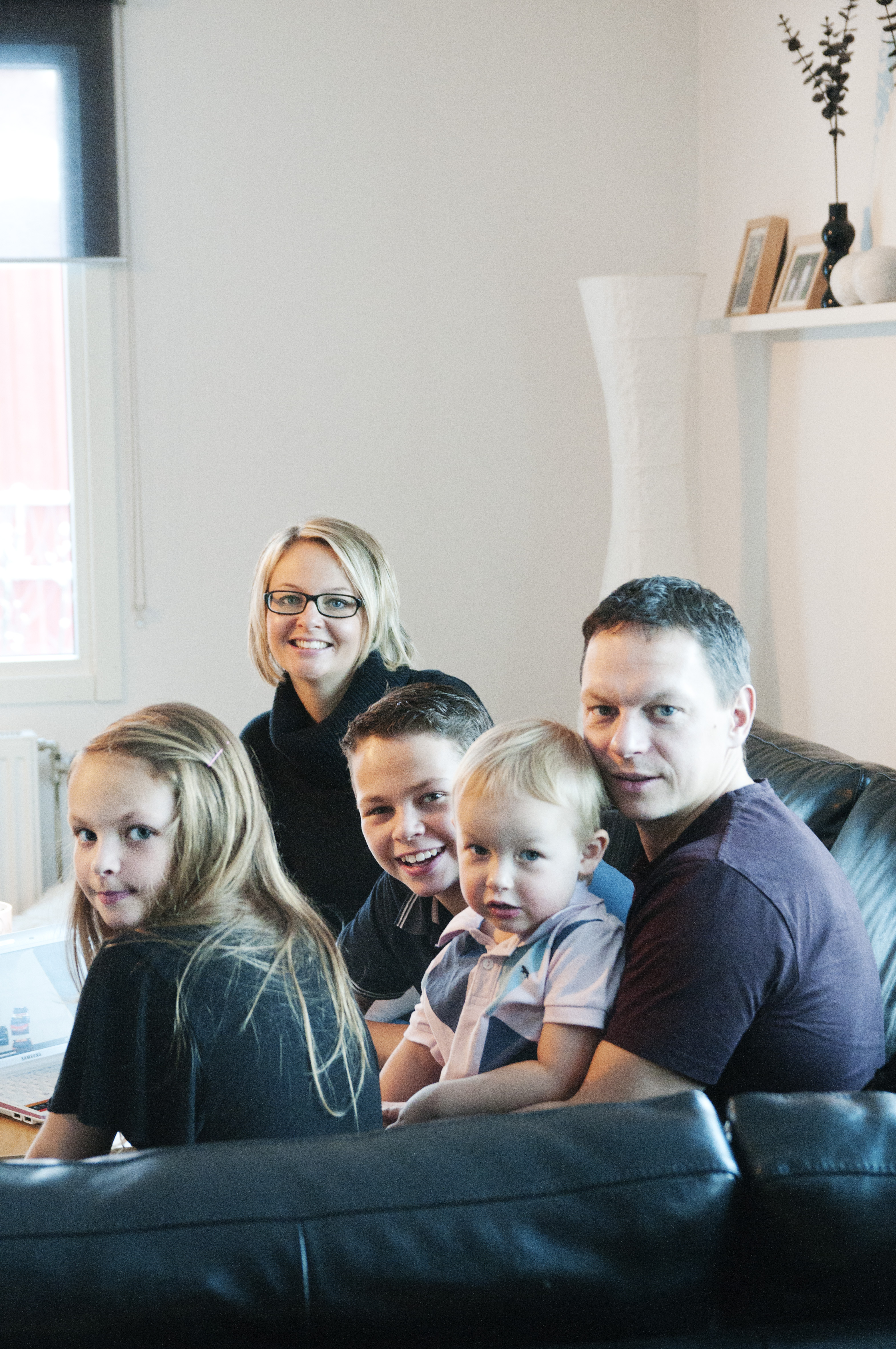 Familj sitter i soffa och ler mot kameran