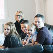 Familj sitter i soffa och ler mot kameran