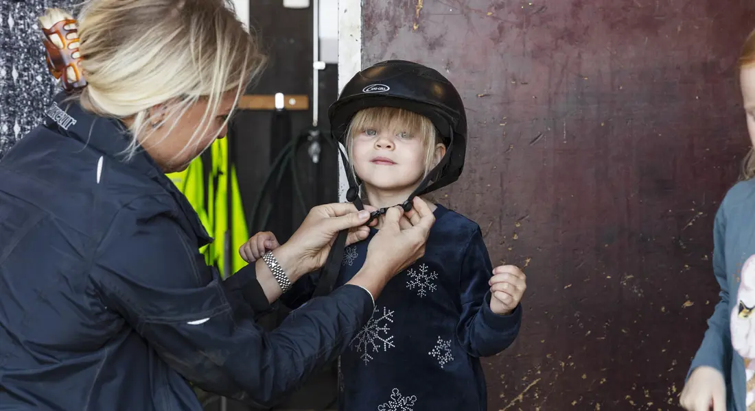 En ljushårig kvinna sätter på en hjälm på en liten flicka