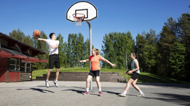 En kille och två tjejer spelar basket utomhus