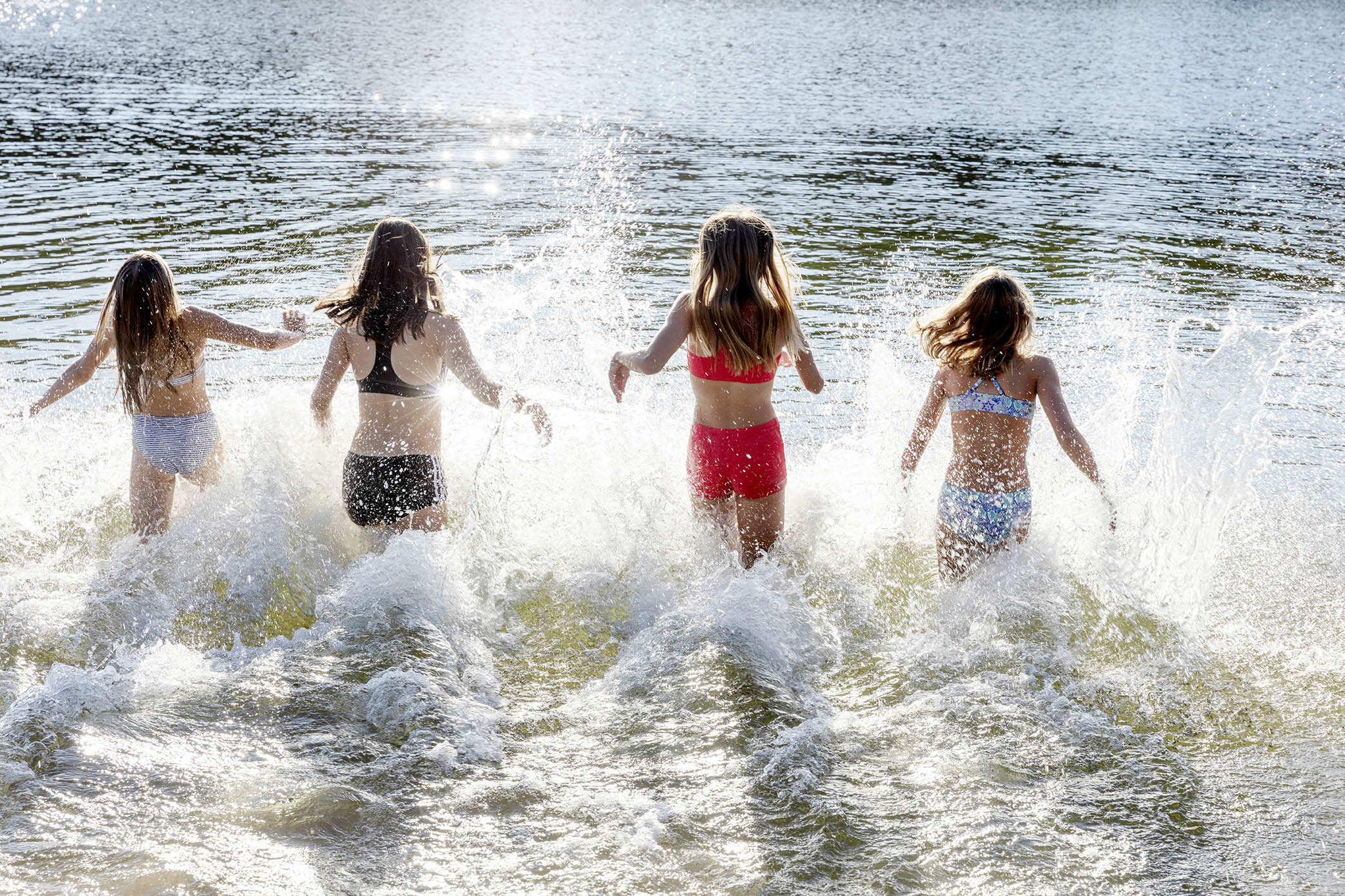 Fyra flickor i badkläder springer ned i vattnet 
