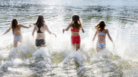 Fyra flickor i badkläder springer ned i vattnet 