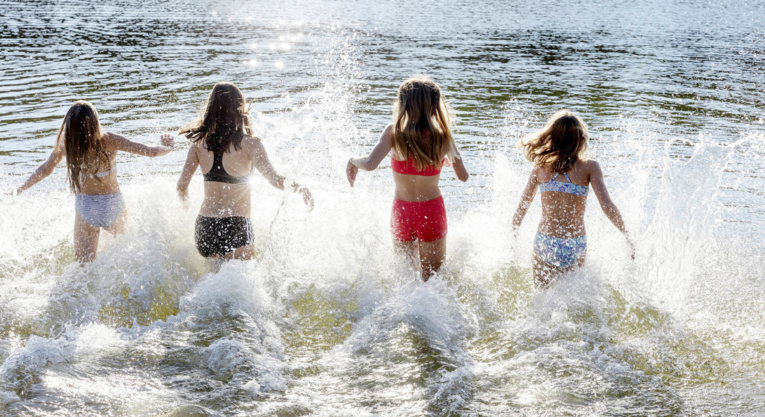 Fyra flickor i badkläder springer ned i vattnet 