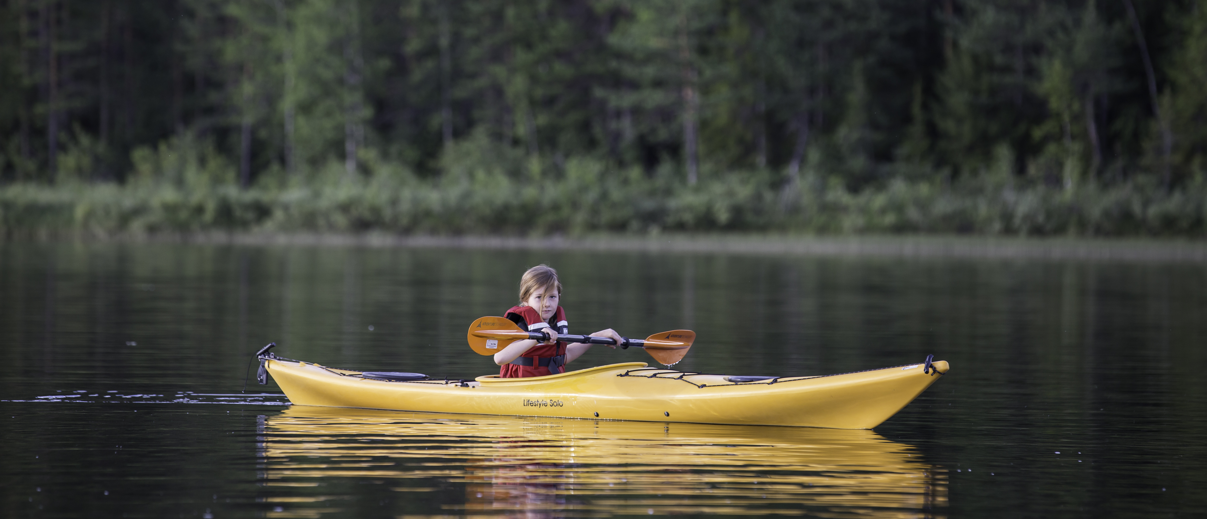 Flicka paddlar en gul kajak på lugnt vatten