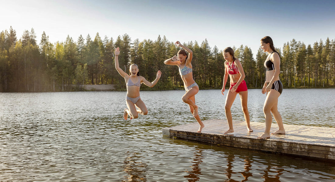 Fyra flickor på en brygga, två hoppar ned i vattnet