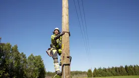 Montör klättrar i elstolpe med varselkläder och hjälm
