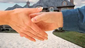 Två händer som skakar hand, hus i bakgrunden. Foto