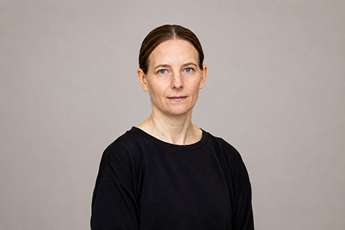 Kvinna i svart tröja och uppsatt hår tittar in i kameran