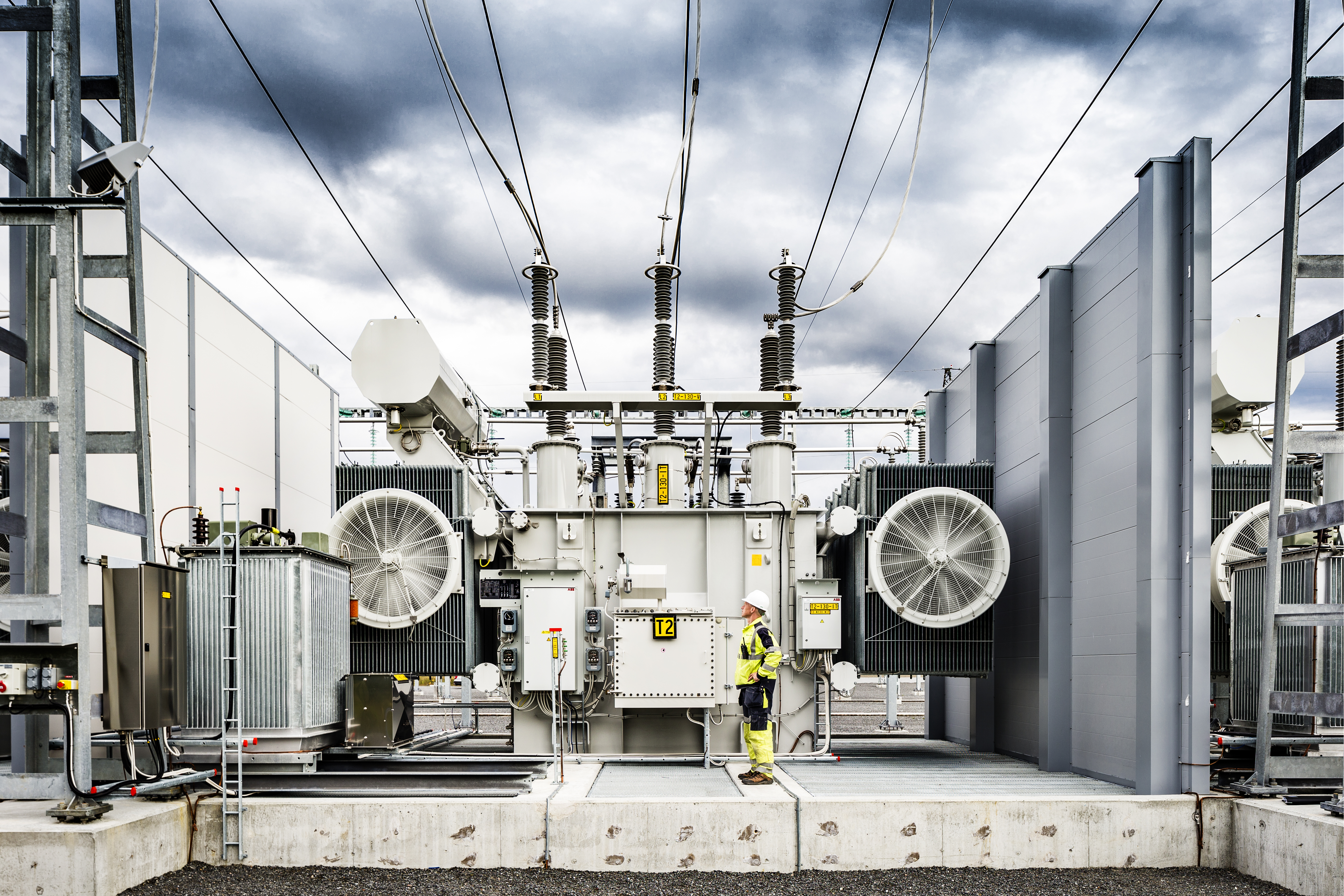 Man med gula arbetskläder och vit hjälm står vid ett ställverk. Foto